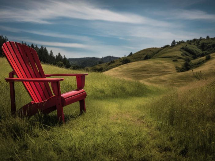 Red Adirondack chair in a grassy field of hills with blue sky- peaceful scene