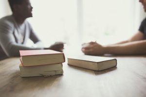 two people drinking coffee at a table stack of books in the foreground