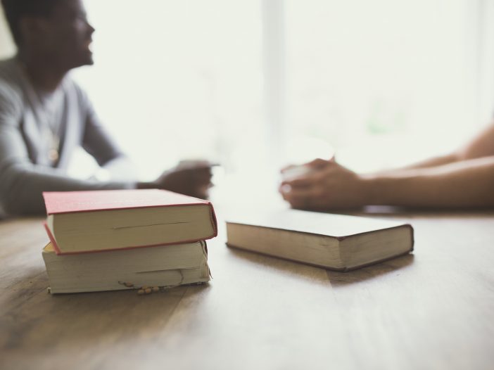 two people drinking coffee at a table stack of books in the foreground