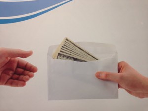 Envelope of 100 dollar bills being handed from one person to another.