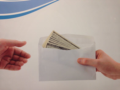 Envelope of 100 dollar bills being handed from one person to another.