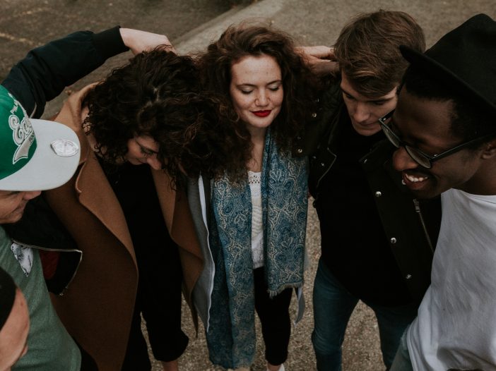 Group of people of different genders and races with their arms around each other on the sidewalk