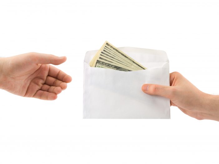 Envelope of 100 dollar bills being handed from one person to another.