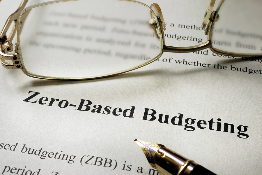 Shows a person's glasses and pen with the words zero based budgeting on the paper underneath