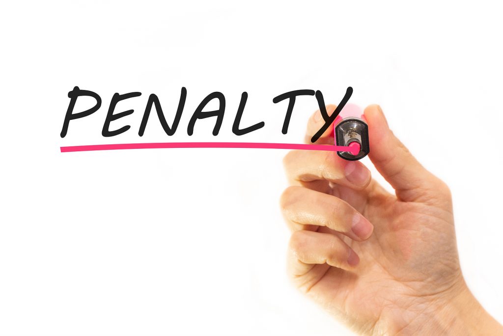 A hand writing the word penalty in black text with red underline. 