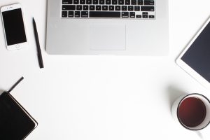 Shows a laptop, coffee, pens, and other items found on a desk.