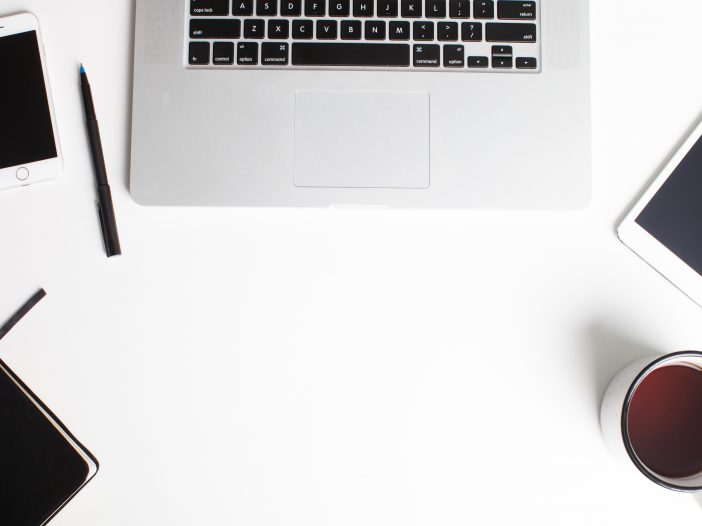 Shows a laptop, coffee, pens, and other items found on a desk.